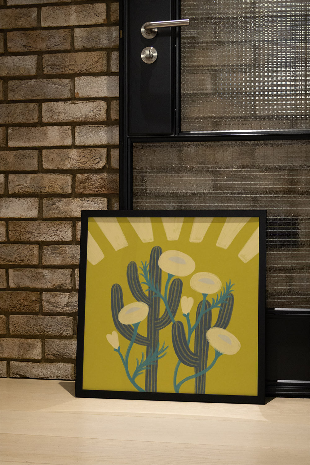 "Sunrise Cactai" by Sophia Sky in black frame, displayed in styled interior with cactus-themed art print. |type=lifestyle|
